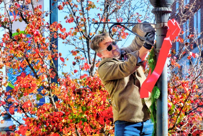 Tony Hampton tightens one of 100 red bows, donated by Charles A. Schaefer Flower Shop. More than 50 volunteers spread out through the Continental Square area of downtown York on Sunday, Nov. 19. 2023, for the annual Hanging of the Greens, organized by Downtown Inc. Bil Bowden photo