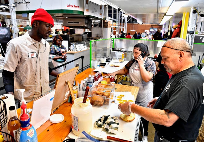 Aaliyah Jamison, back, takes a call while Robert Merced, right, of The Breakfast Store, assists customer Ronnie Brown, of York City, at Penn Market in York City, Saturday, Feb. 17, 2024. (Dawn J. Sagert/The York Dispatch)