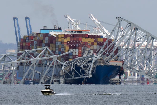 A boat moves past a container ship as it rests against wreckage of the Francis Scott Key Bridge on Tuesday, March 26, 2024, as seen from Pasadena, Md. The container ship lost power and rammed into the major bridge in Baltimore early Tuesday, causing it to snap and plunge into the river below. Several vehicles fell into the chilly waters, and rescuers searched for survivors. (AP Photo/Mark Schiefelbein)